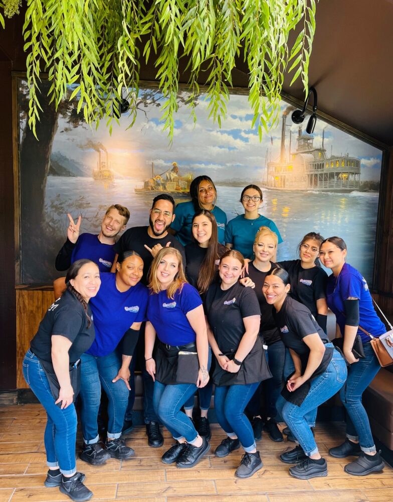 A group of people posing in front of a large painting of a bayou.